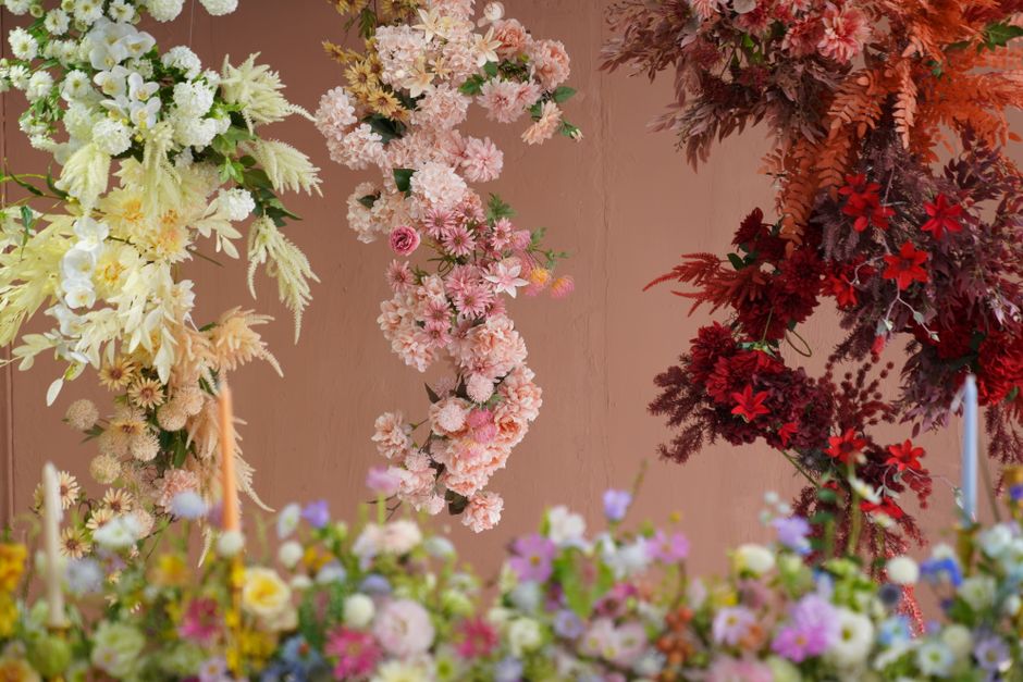 A vibrant floral arrangement featuring a mix of freshly cut flowers placed closely together. The bouquet includes clusters of red and pink flowers with small, rounded petals, alongside bright orange d