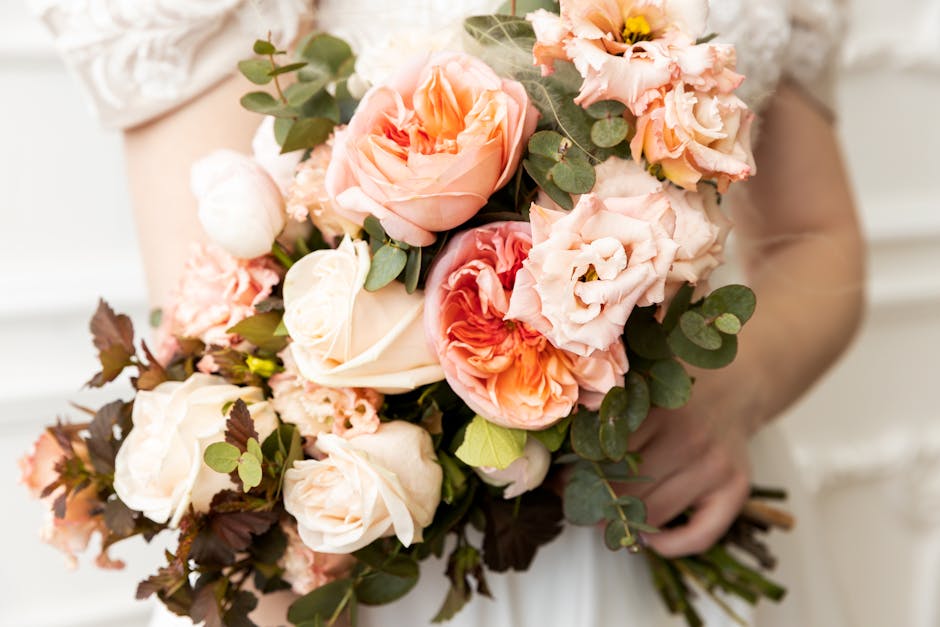 A florist from flowersbyflorists.co.uk holds a vibrant floral bouquet featuring large pink gerbera daisies, soft pink spray roses, white daisies with yellow centers, and delicate pink baby's breath, a